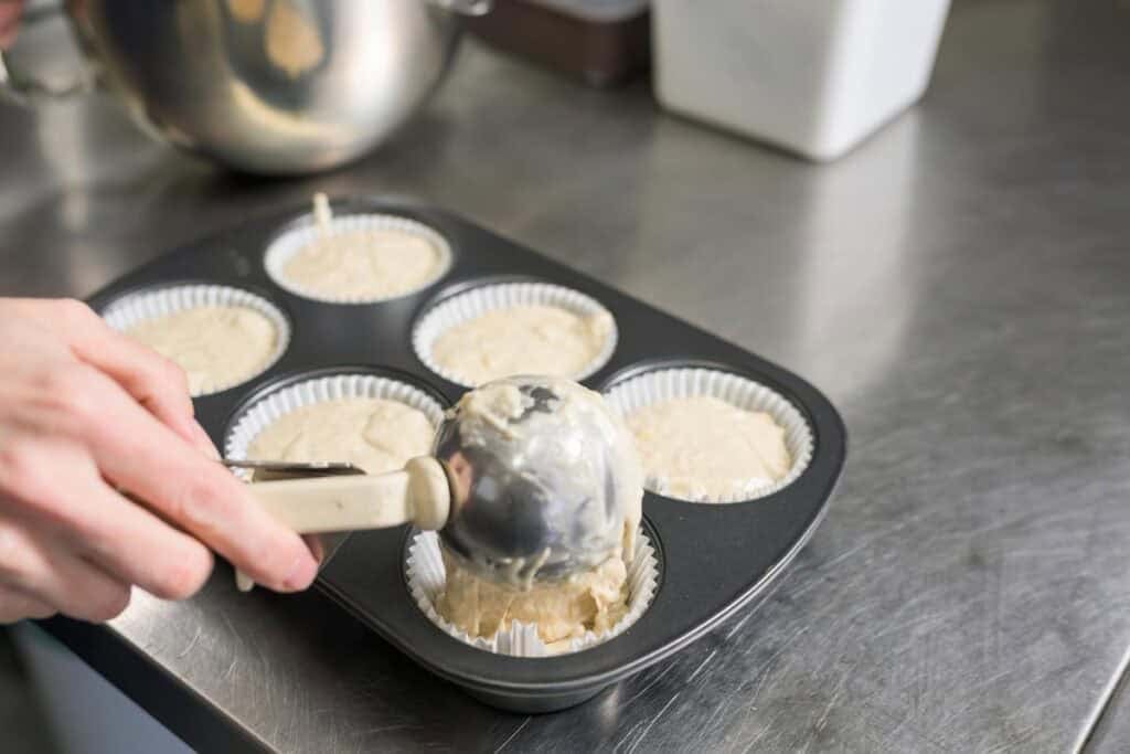 woman scooping muffin batter into tin