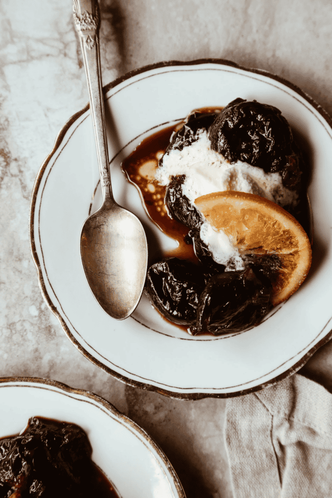 stewed prunes on a plate garnished with a slice of orange