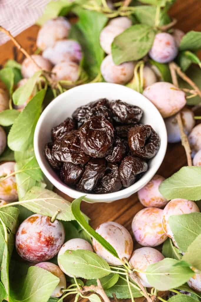 a bowl of dried prunes surrounded by fresh prunes